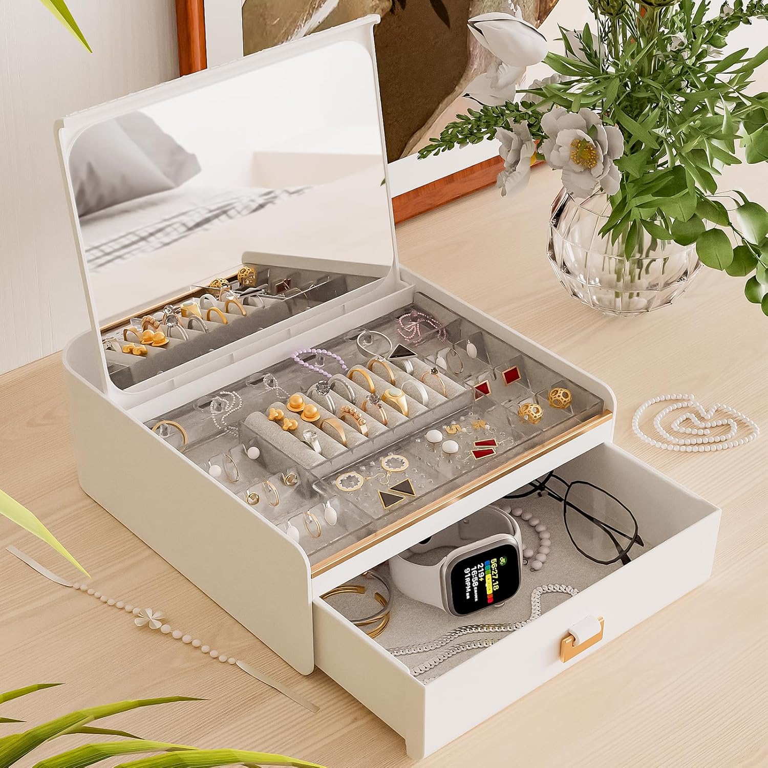 White jewelry organizer with compartments on a wooden surface with plants.