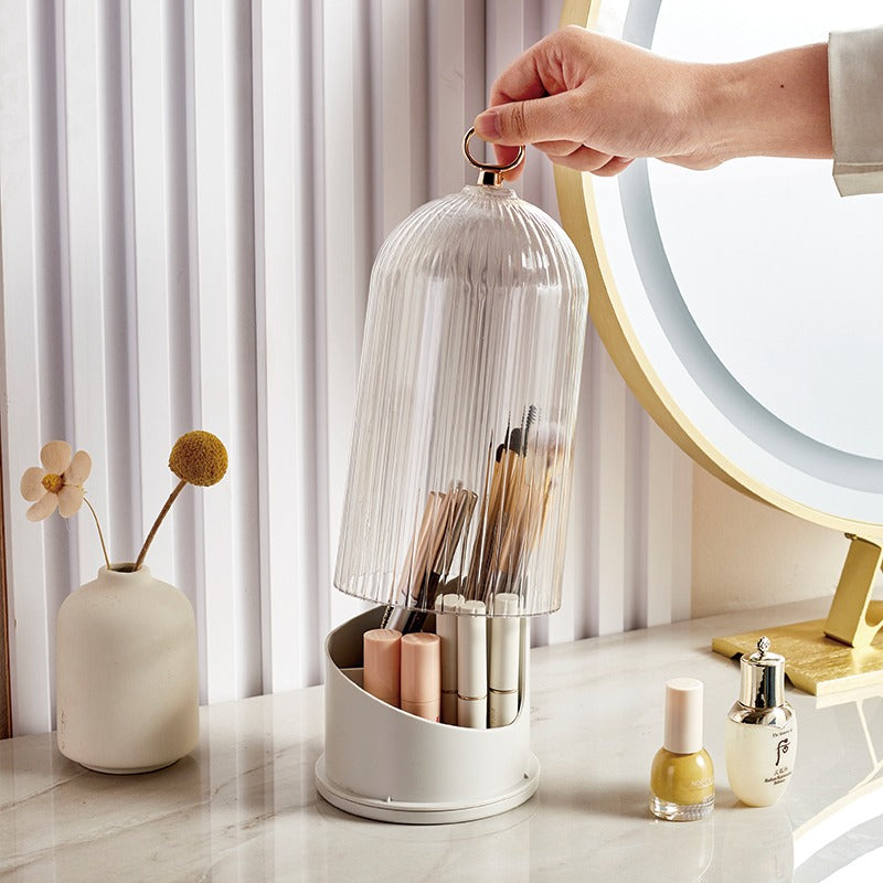 Hand holding a transparent dome over a white organizer with various items on a marble surface.
