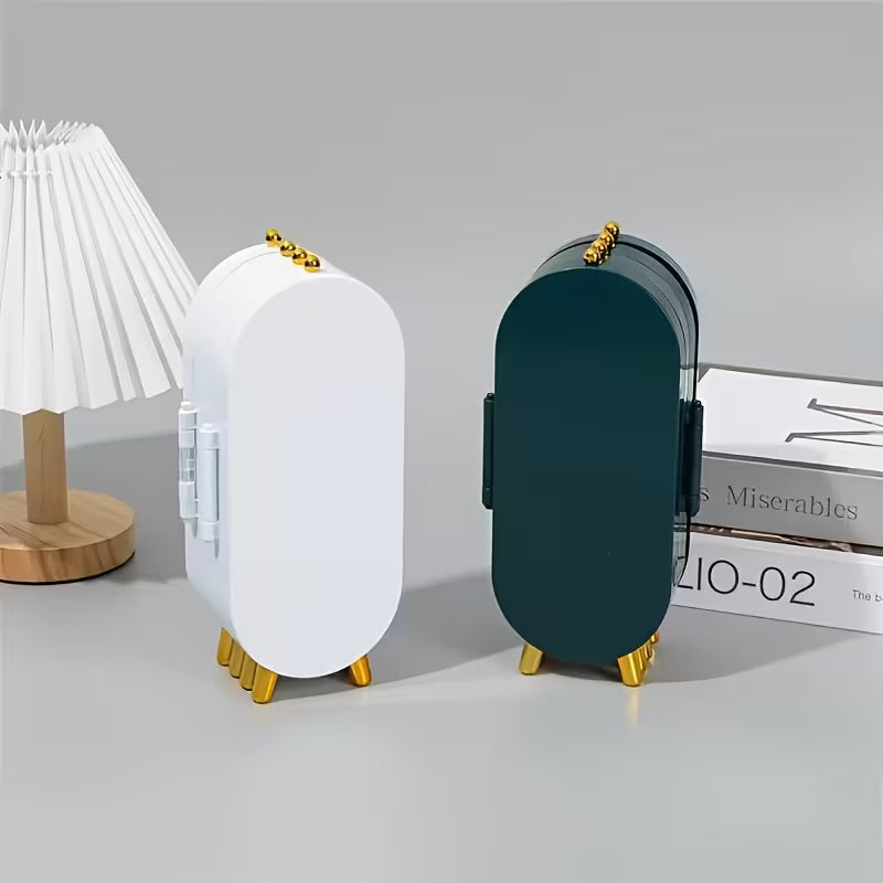 Two oval-shaped containers with gold bases on a gray surface, with a lamp and books in the background.